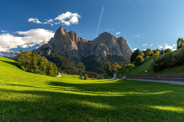 Free photo field surrounded by rocks covered in greenery under a blue sky and sunlight in italy