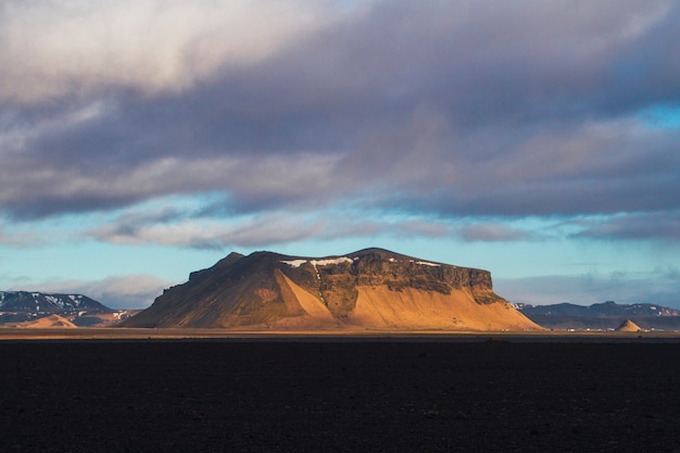 Free photo field surrounded by rocks covered in the snow under a cloudy sky during the sunset in iceland