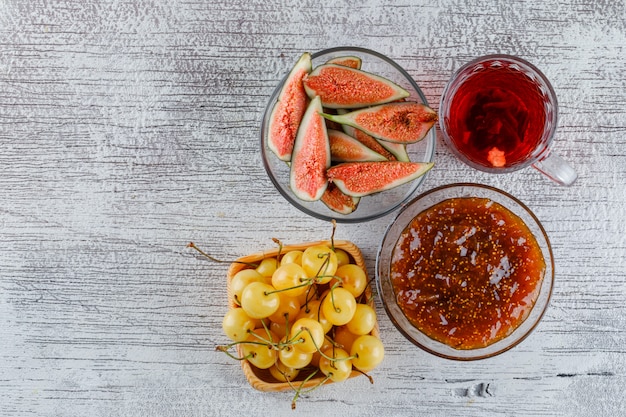 Fig jam with figs, cherries, cup of tea in a bowl on grungy, top view.