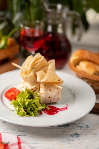 Filled, stuffed lavash with tomato and lettuce salad in white plate