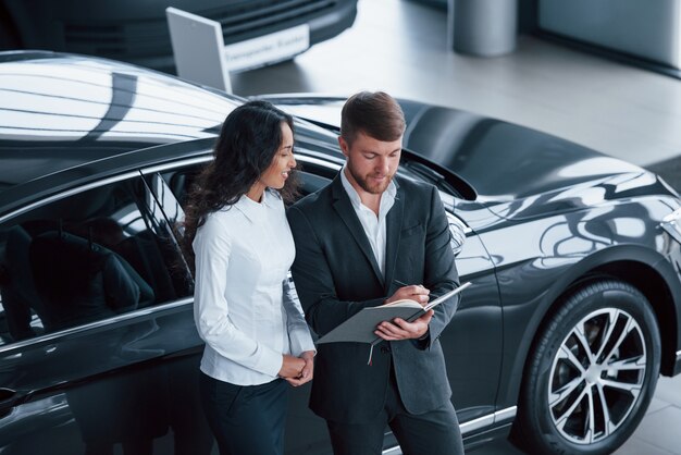 Filling the documents. Female customer and modern stylish bearded businessman in the automobile saloon