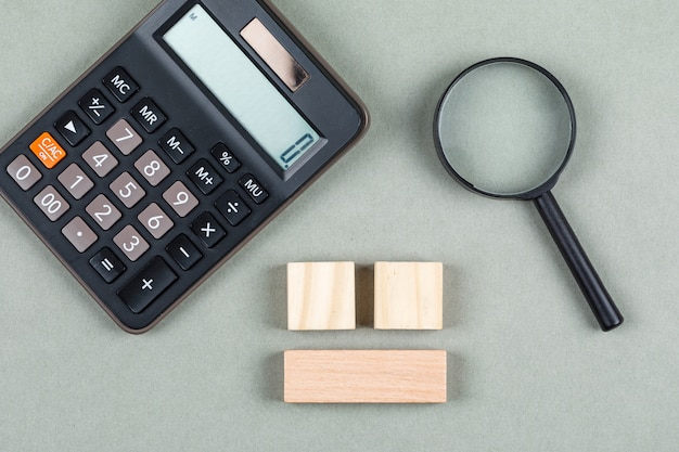 Free Photo financial analysis and accounting concept with magnifier, wooden blocks, calculator on gray background top view. horizontal image