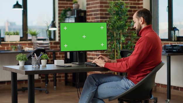 Financial analyst working with green screen on computer, planning business strategy. Office worker using isolated copyspace with mockup template and blank chroma key background. Tripod shot.