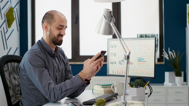 Financial assistant working on smartphone app with statistics, using moible phone to browse internet for business growth strategy. Male employee planning research presentation in office.