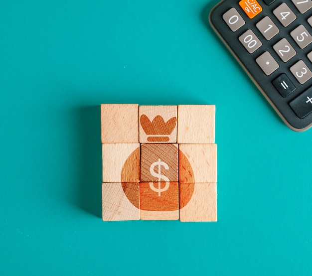 Financial concept with icon on wooden cubes, calculator on turquoise table flat lay.