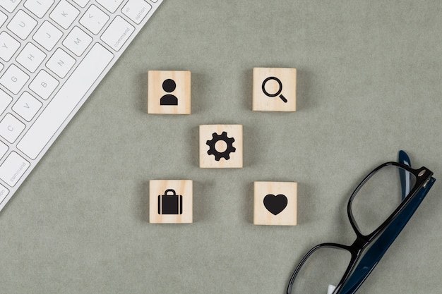 Free photo financial concept with wooden cubes, glasses, keyboard on grey background flat lay.