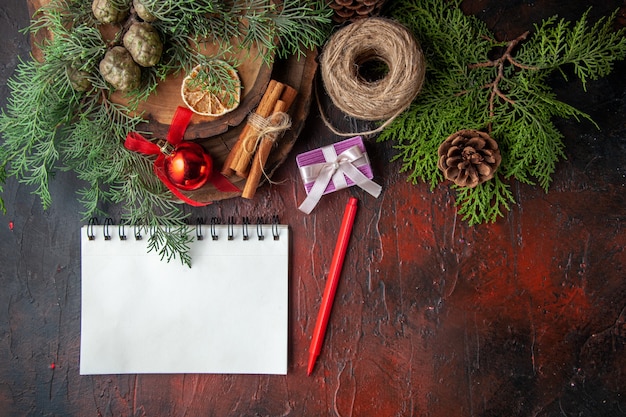 Fir branches and closed spiral notebook with pen cinnamon limes ball of rope on dark background