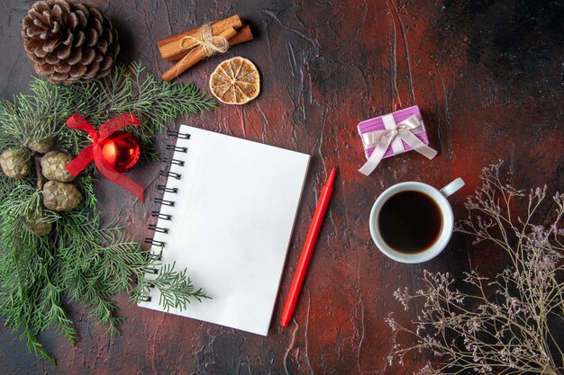 Fir branches and closed spiral notebook with pen cinnamon limes conifer cone and a cup of black tea on dark background