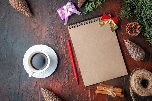 Fir branches decoration accessories conifer cones gift and notebook a cup of black tea on dark background