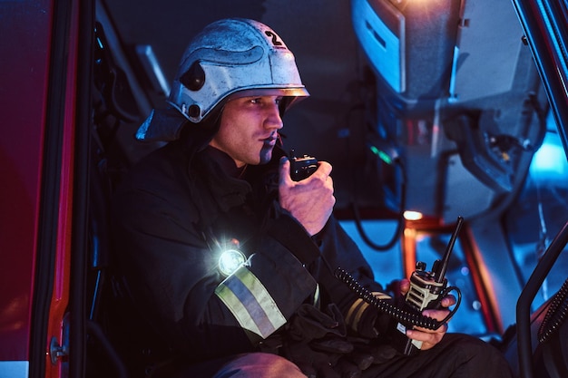 Free Photo the fire brigade arrived at the night-time. fireman in a protective uniform sitting in the fire truck and talking on the radio