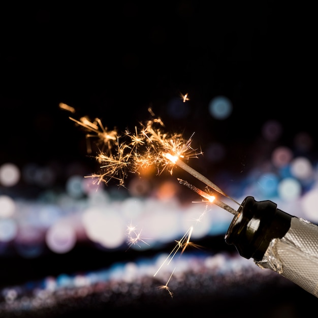 Fire sparkler in champagne bottle on bokeh background at night