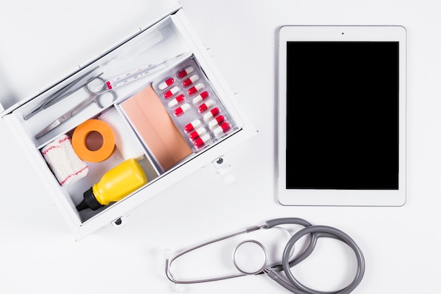 First aid kit with digital tablet and stethoscope on white background