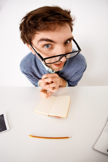 Free photo fish-eye upper-angle shot of funny young male eployee at office desk, wear glasses, staring thoughtful and interested, creating new content, writing down ideas in notebook