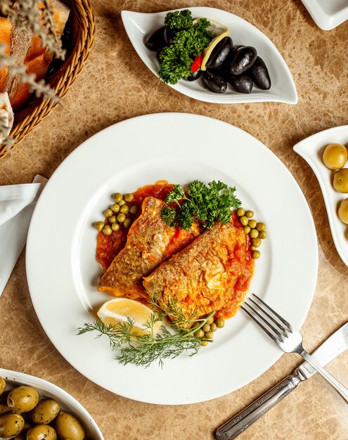 Fish fillets in tomato sauce served with peas lemon and herbs