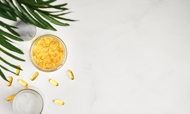 Fish oil capsules with omega 3 and vitamin D in a glass jar on a white concrete surface