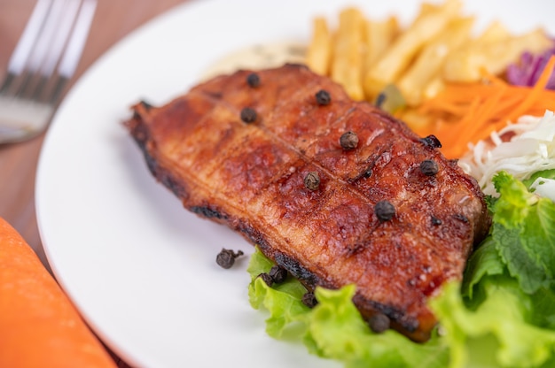 Free photo fish steak with french fries, kiwi, lettuce, carrots, tomatoes, and cabbage in a white dish.