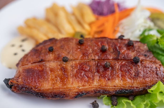 Free photo fish steak with french fries, kiwi, lettuce, carrots, tomatoes, and cabbage in a white dish.