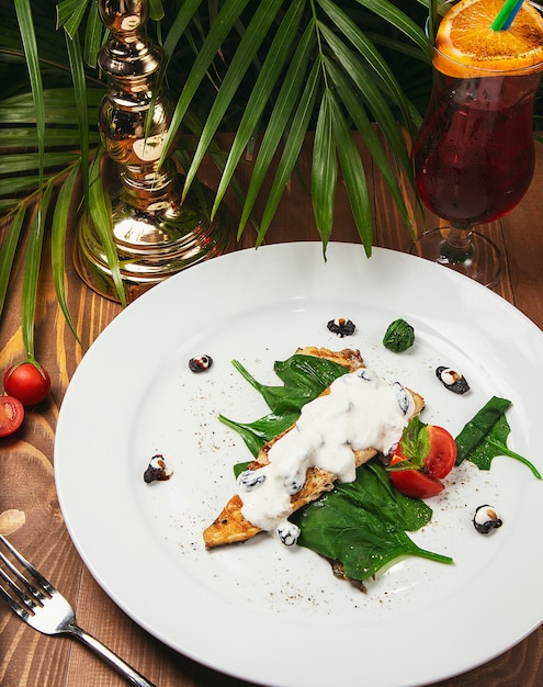 Fish stew in a creamy sauce, tomato, parsley on the plate, knife, fork light wooden table