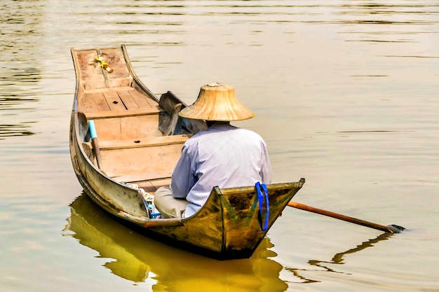 Fisherman in an Asian cone hat sailing in the lake with a small wooden boat