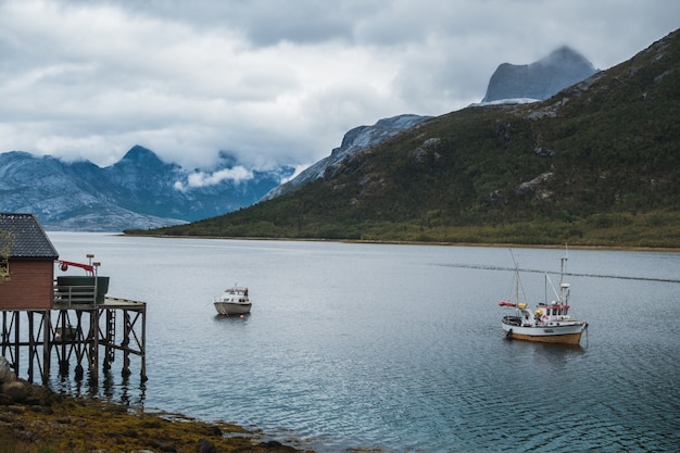 fishing boats sailing in the lake near the mountains under the cloudy sky