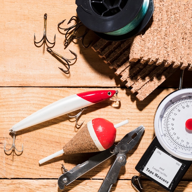 Fishing lure; float; hook with plier and fishing reel on measuring scale over the desk