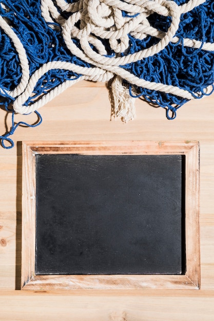 Free photo fishing net over the blank blackboard over the wooden surface