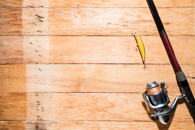 Free photo fishing rod with yellow fishing bait on wooden plank