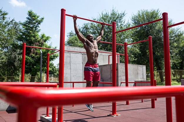 The fit athlete doing exercises at stadium. Afro or african american man outdoor at city. Pull up sport exercises. fitness, health, lifestyle concept