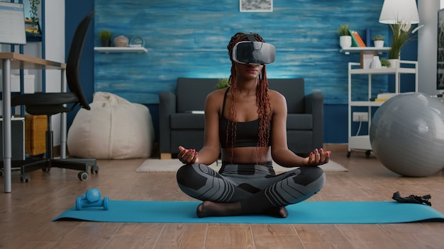 Free photo fit black woman wearing virtual reality headset while sitting on yoga map