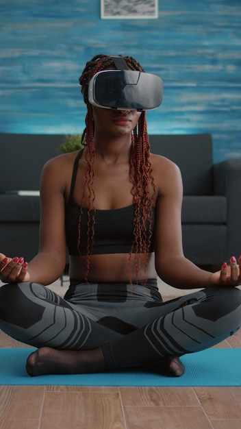 Free photo fit black woman wearing virtual reality headset while sitting on yoga map