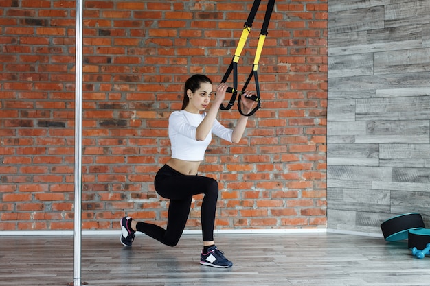 Fit young woman does stretching, push up and pull up on the gymnastics rings in gym