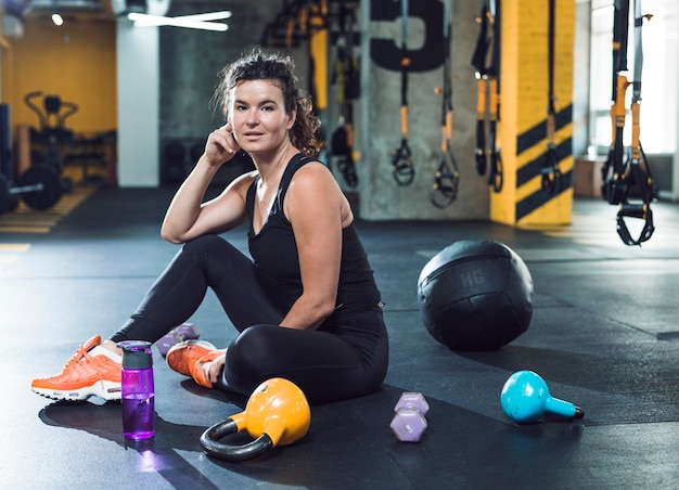 Free Photo fit young woman sitting on floor near exercise equipments in gym