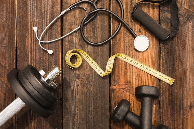 Free photo fitness equipment with stethoscope and measuring tape on wooden surface