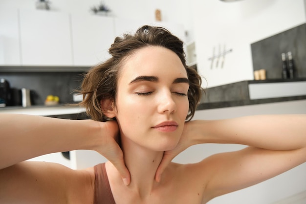 Fitness girl in activewear doing yoga at home stretching and working out massaging her neck with ple