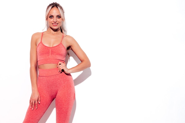 Free photo fitness smiling woman in pink sports clothing young beautiful model with perfect bodyfemale posing near white wall in studiocheerful and happy stretching out before training