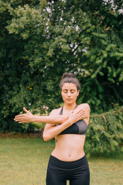 Fitness woman warm up by stretching arms before exercises at the park