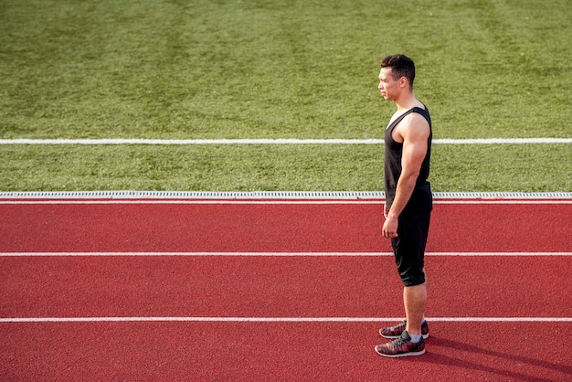 Fitness young male runner standing on red running track