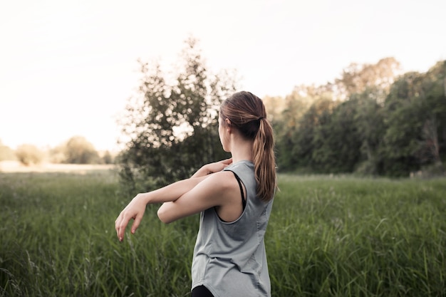 Free photo fitness young woman stretching her hand standing in green grass