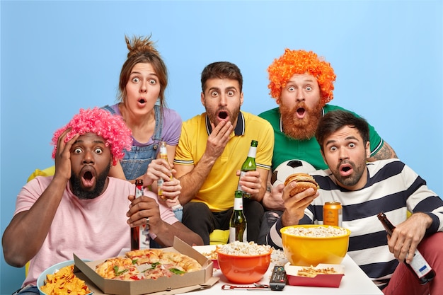 Five diverse friends stare with shock at TV set