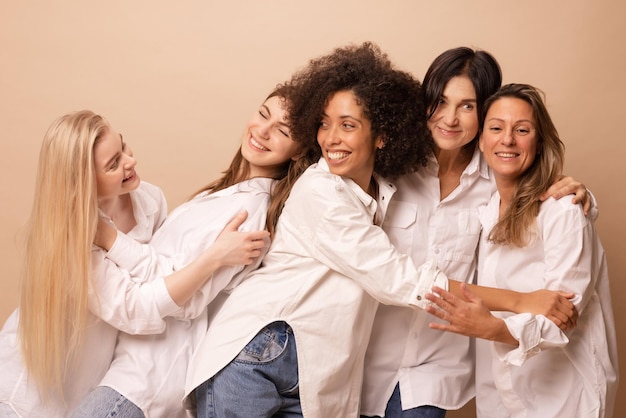 Free photo five diverse interage women wearing white shirts and jeans are having fun against beige background lifestyle friendship and people concept