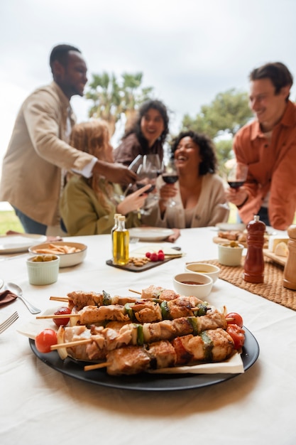 Free Photo five friends toasting with glasses of wine and eating barbeque during outdoor party