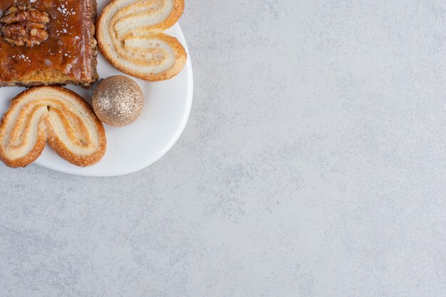 Flaky cookies and a bakhlava on a platter with a bauble on marble surface