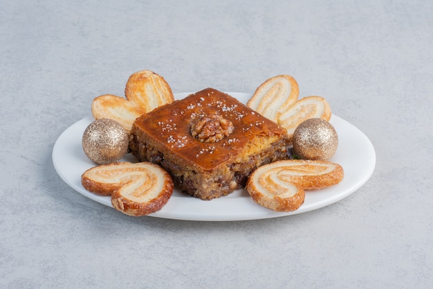 Flaky cookies and a bakhlava on a platter with a bauble on marble surface