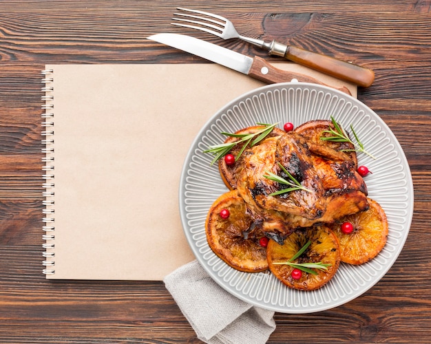 Free Photo flat lay baked chicken and orange slices on plate with cutlery and blank notebook