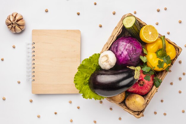 Flat lay of basket of fresh vegetables with notebook