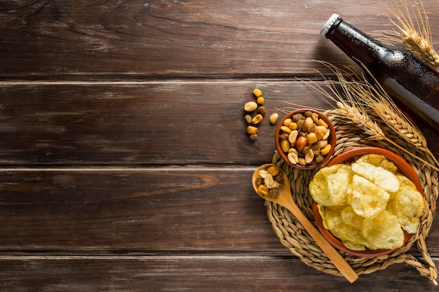 Flat lay of beer bottle with chips and nuts