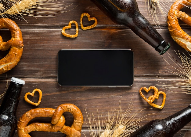 Free photo flat lay of beer bottle with pretzels and smartphone