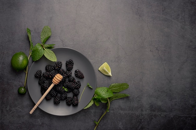 Flat lay of blackberries on plate with limes and honey dipper