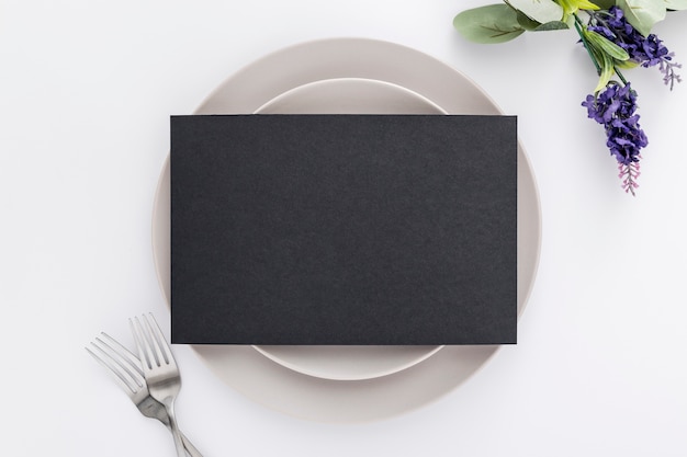 Flat lay of blank menu paper on plates with forks and flowers