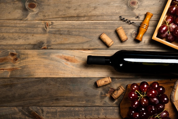 Flat lay of a bottle of wine surrounded by corks and red grapes